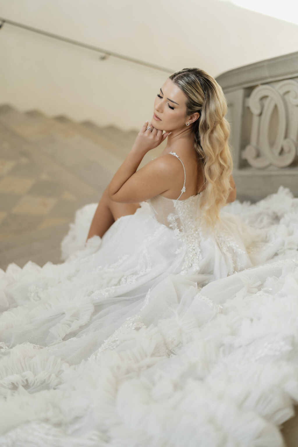 Braut sitzt auf einer Treppe, ihr Kleid verteilt sich auf den Stufen, wunderschönes Hochzeitskleid