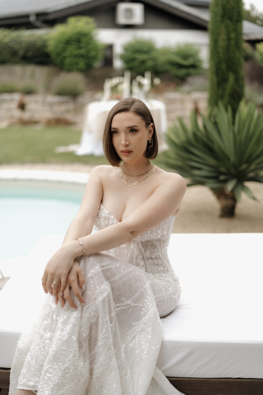 Porträt der Braut, sitzend, blickt ernst in die Kamera, im Hintergrund Pool und Hochzeitsdekoration