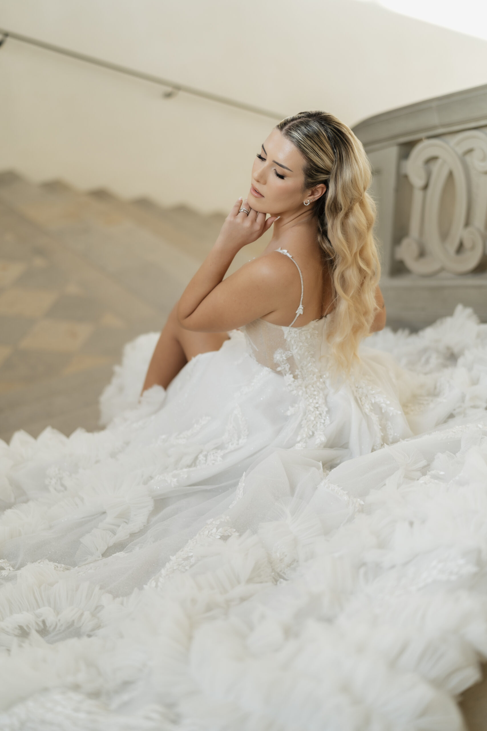 Braut sitzt auf einer Treppe, ihr Kleid verteilt sich auf den Stufen, wunderschönes Hochzeitskleid