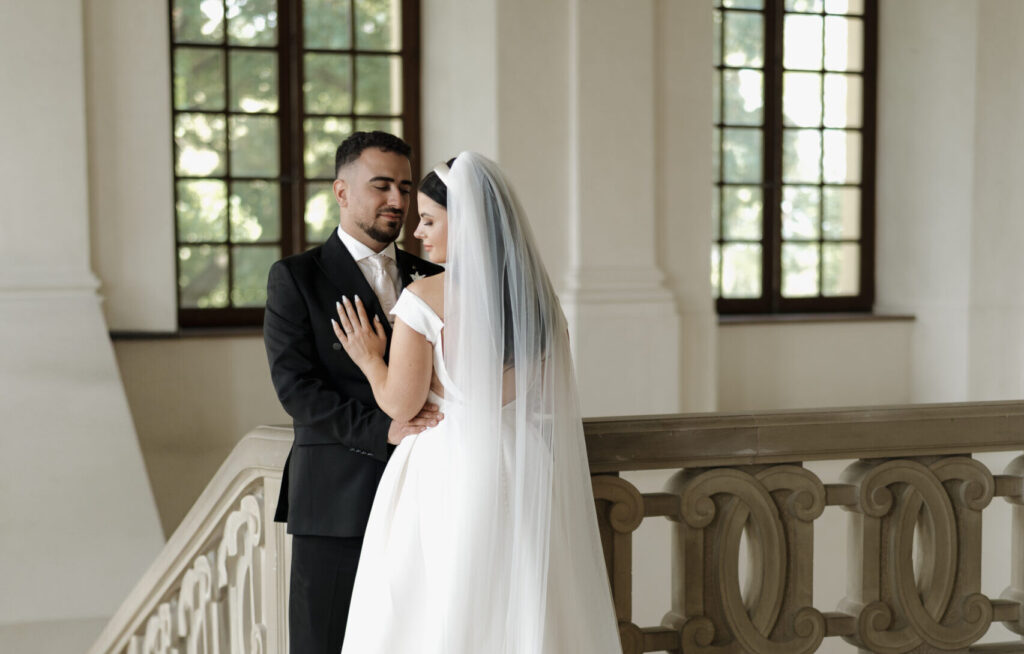 Brautpaar steht eng beieinander im Schloss Dachau, die Braut blickt über ihre Schulter, während der Bräutigam sie bewundernd anschaut – romantische Hochzeitsfotografie