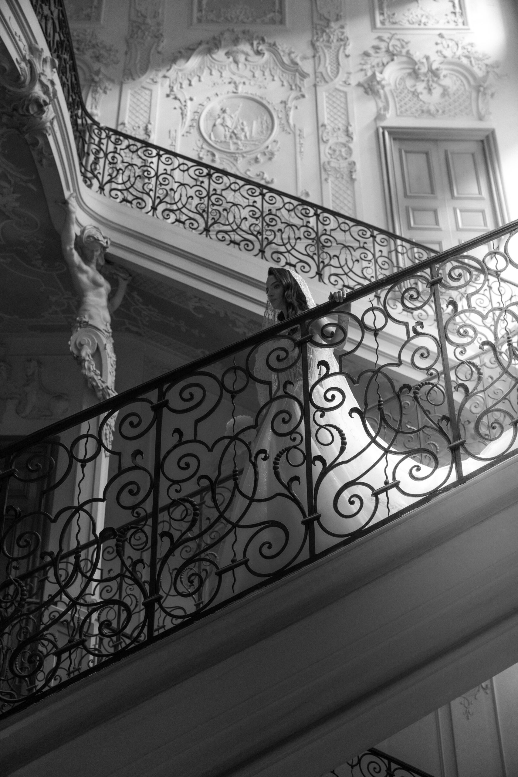 Braut geht die Treppe hinunter, stützt sich am Geländer, im Schwarz-Weiß-Porträt