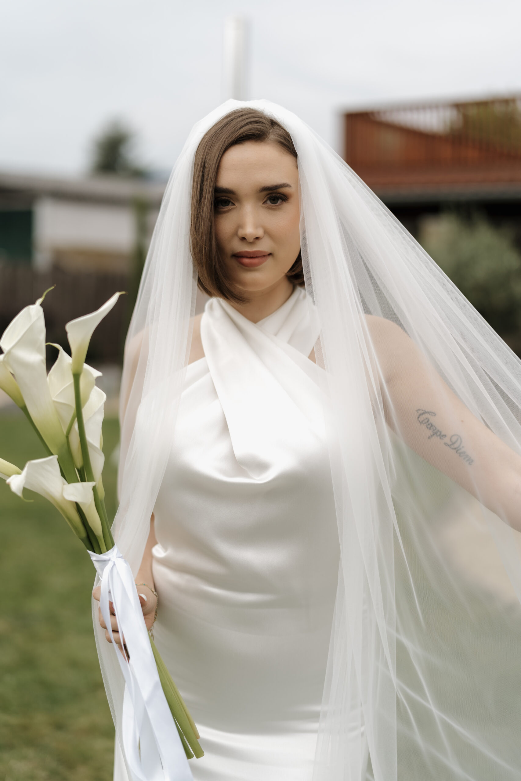 Braut in hochwertigem Brautkleid mit langer Schleppe hält einen eleganten Brautstrauß aus Calla-Lilien – stilvolle Hochzeitsfotografie