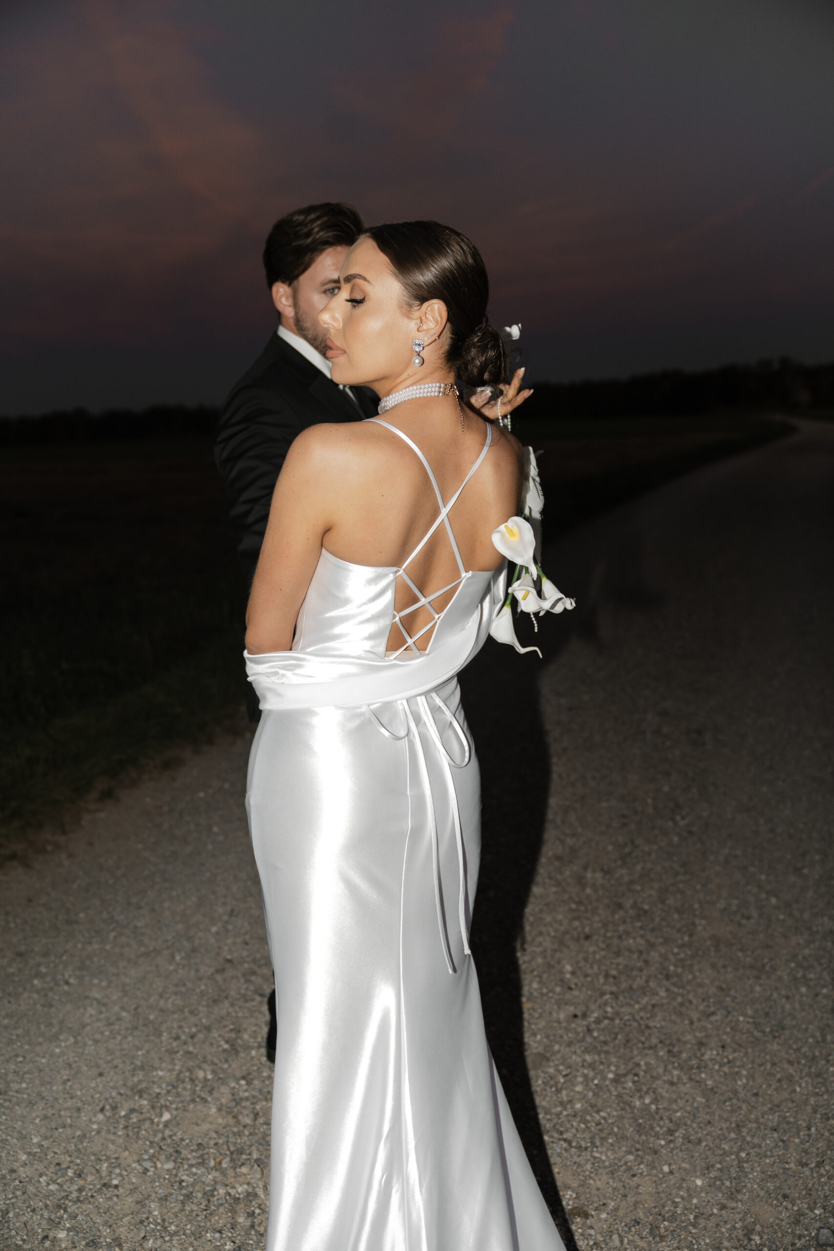 Stylisches Brautpaar, Braut hält Blumen über den Rücken, Aufnahme mit dunklem Hintergrund und Blitzlicht