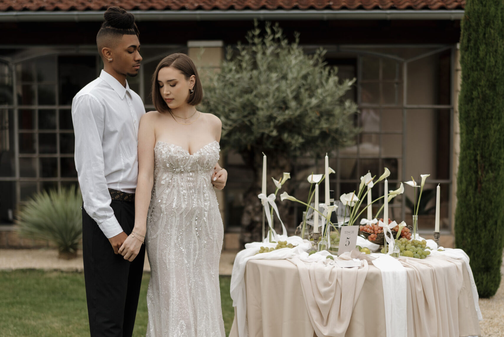 Brautpaar hält sich die Hände, Bräutigam legt seine Hand an die Hüfte der Braut und schaut sie liebevoll an