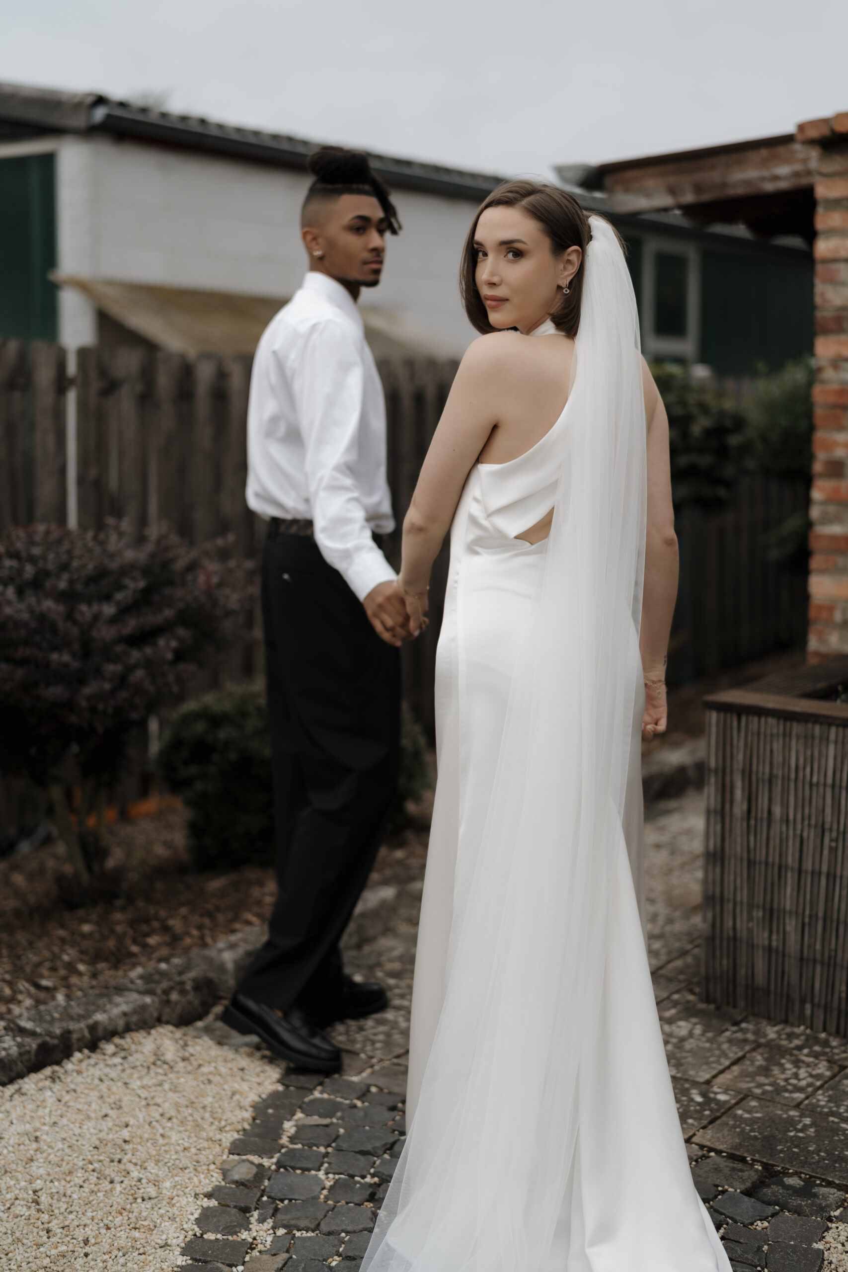 Braut blickt selbstbewusst in die Kamera im eleganten Hochzeitskleid, während der Bräutigam sie bewundernd anschaut