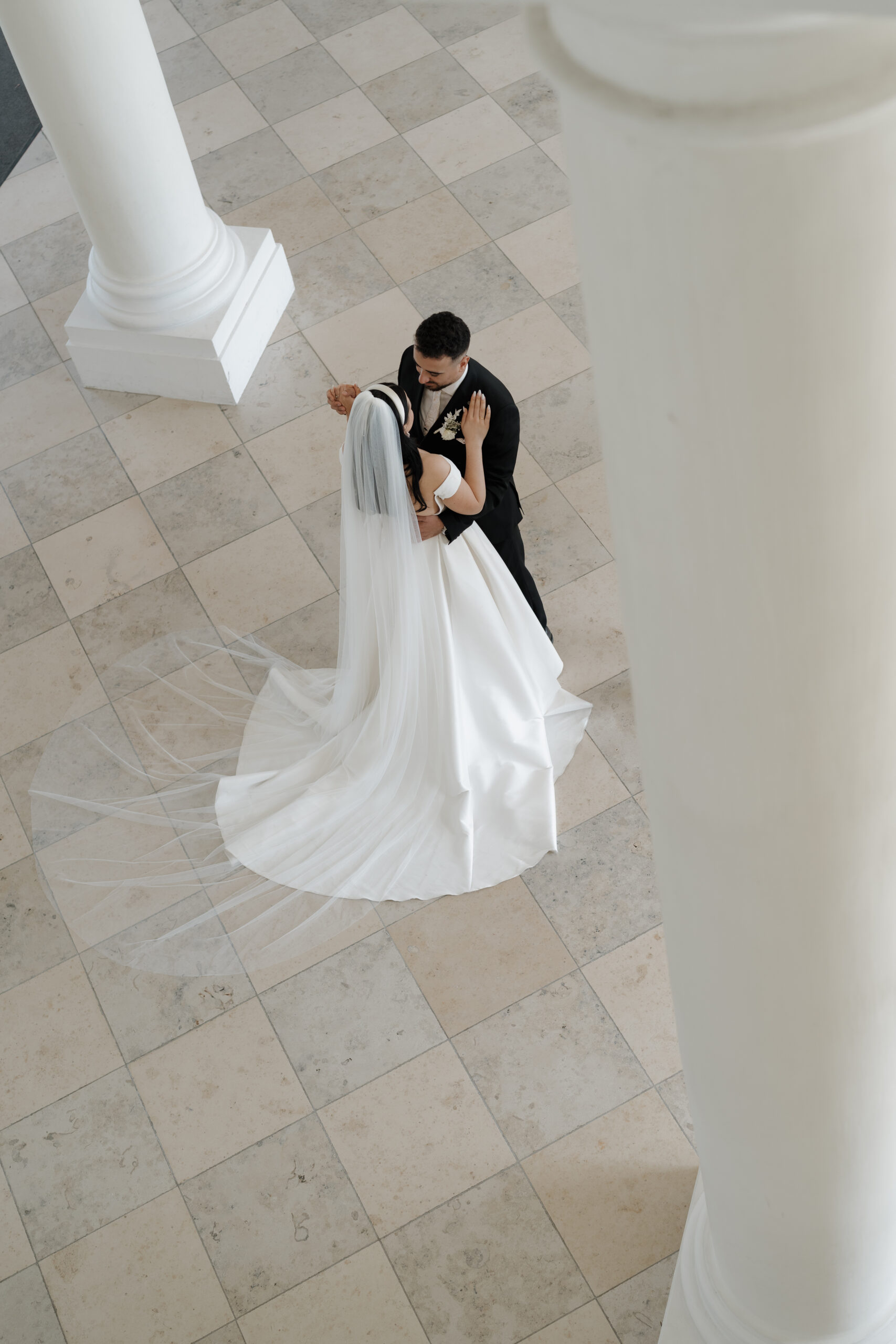 Brautpaar steht zwischen hohen Säulen im Schloss in Tanzposition und schaut sich voller Liebe an