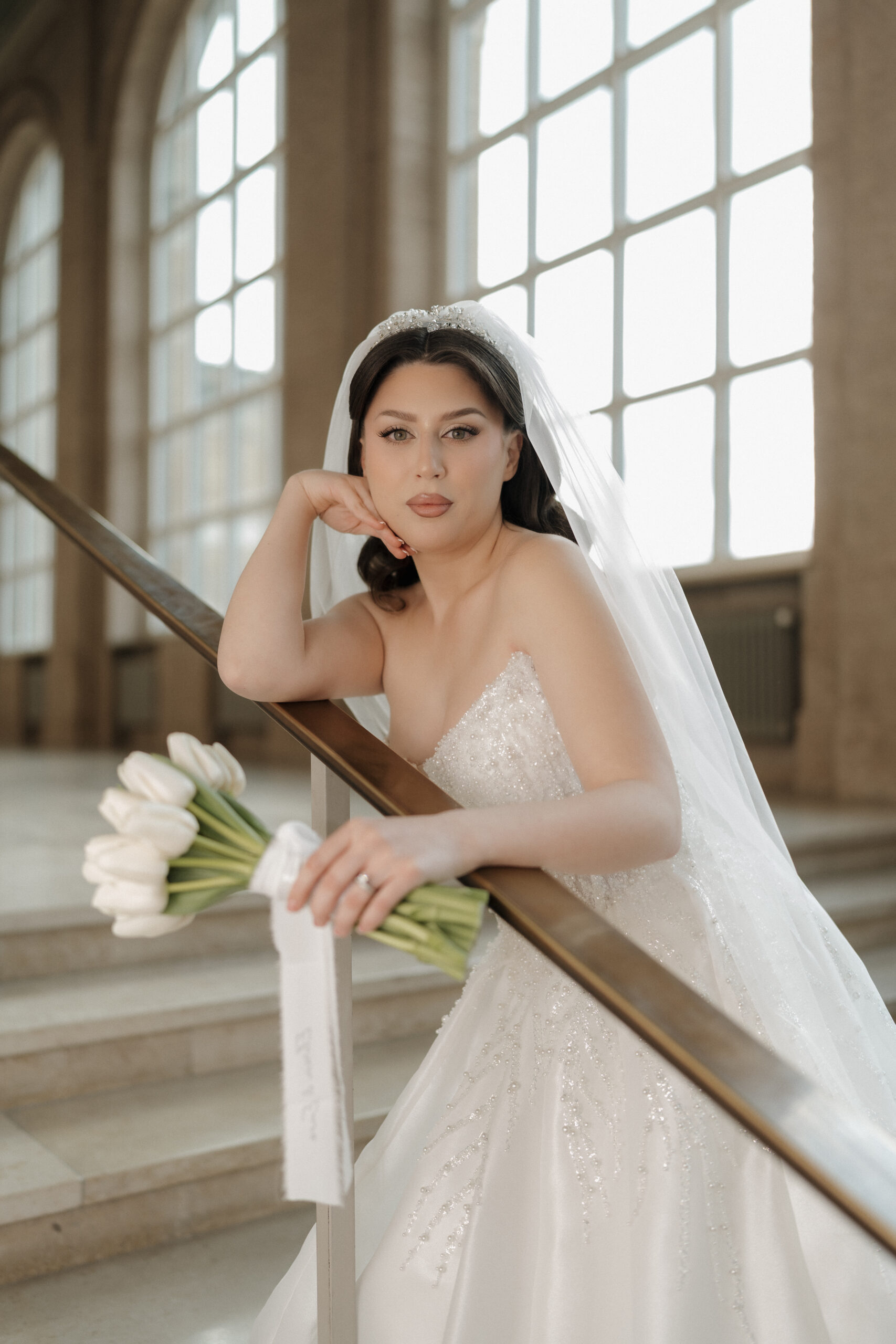 Braut posiert elegant auf einem Geländer und hält ihren Blumenstrauß